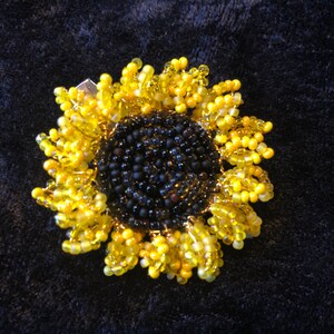May include: A beaded sunflower brooch with a black center and yellow petals.