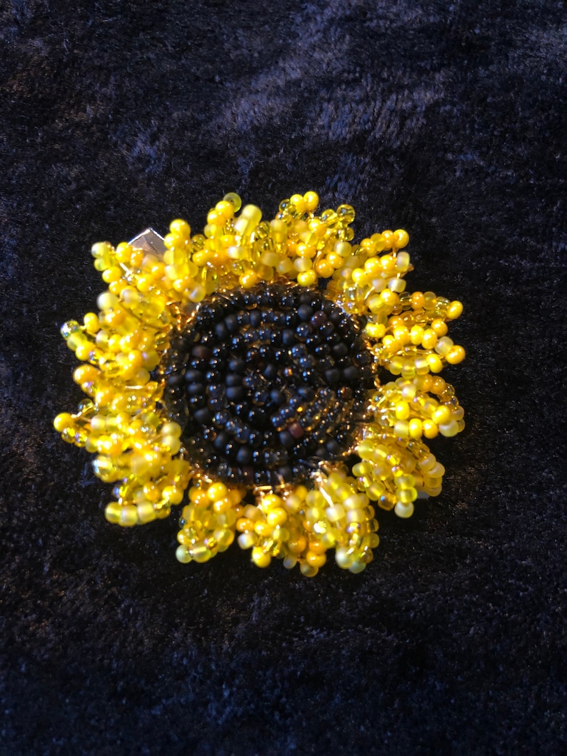 May include: A beaded sunflower brooch with a black center and yellow petals.