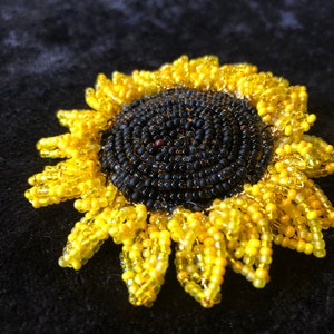 May include: A beaded sunflower brooch with a black center and yellow petals.