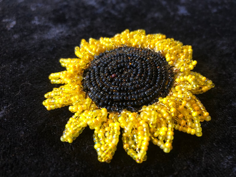 May include: A beaded sunflower brooch with a black center and yellow petals.