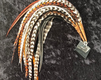 May include: A decorative arrangement of feathers in shades of brown, orange, white, and grey, attached to a copper-coloured metal piece. The feathers are curved, and a small black square is attached to the metal.