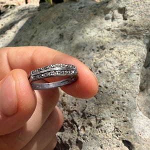 May include: A silver-toned ring featuring two parallel rows of small, dark, faceted stones set along the band. The interior of the band is clearly stamped with the word SILVER and the number 925, indicating the metal composition of the jewelry piece.