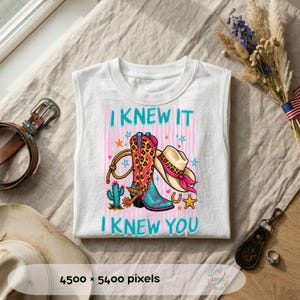 Puede incluir: Una camiseta blanca sin mangas con un estampado gr&aacute;fico de una bota de vaquero con estampado de leopardo, un sombrero de vaquero beige con una banda rosa, un cactus, un lazo y estrellas. El texto I KNEW IT I KNEW YOU est&aacute; impreso en azul cerceta.