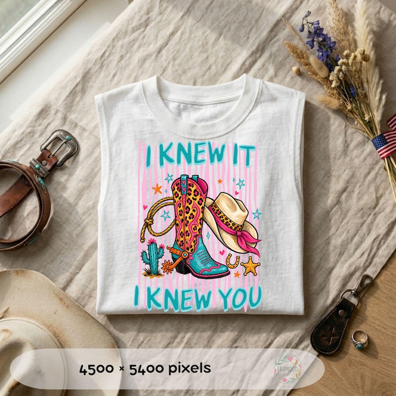 Puede incluir: Una camiseta blanca sin mangas con un estampado gr&aacute;fico de una bota de vaquero con estampado de leopardo, un sombrero de vaquero beige con una banda rosa, un cactus, un lazo y estrellas. El texto I KNEW IT I KNEW YOU est&aacute; impreso en azul cerceta.