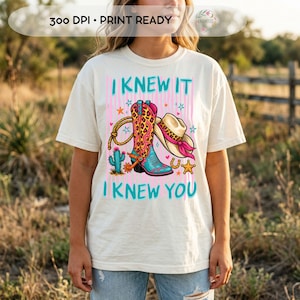 Puede incluir: Una camiseta de manga corta color crema con un estampado gr&aacute;fico que incluye el texto I KNEW IT I KNEW YOU. El dise&ntilde;o muestra una bota de vaquero con estampado de leopardo, un sombrero con una banda rosa, un lazo, un cactus, una herradura y estrellas.