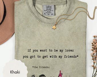 May include: A khaki crew neck t-shirt with the text 'if you want to be my lover you got to get with my friends*' and '*the friends:' above illustrations of five black cats, one holding a wine bottle. The shirt has a Comfort Colors label.