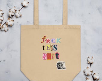 May include: A beige canvas tote bag featuring a ransom note style graphic with the text f*ck this SHiT in various colors and fonts, accompanied by a small black and white photograph of a cat face positioned below the text on the front panel.