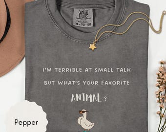 May include: A charcoal gray t-shirt with the white text "I'M TERRIBLE AT SMALL TALK BUT WHAT'S YOUR FAVORITE ANIMAL?" and a graphic of a white goose wearing sunglasses while riding a blue skateboard. The shirt features a Comfort Colors brand label.