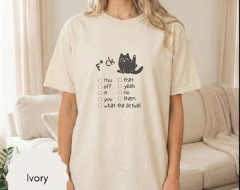 May include: Ivory-colored t-shirt with a black cat graphic and the text "F*ck" above a checklist. The checklist includes options like "this," "that," "off," and "yeah." The shirt is a casual, short-sleeved style.