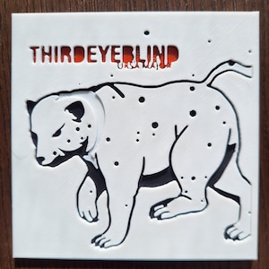 May include: A white square with a 3D-printed design featuring a stylized leopard with black spots and outlines. The text "THIRDEYEBLIND" is above the leopard, with "URSA MAJOR" below it, both in red.