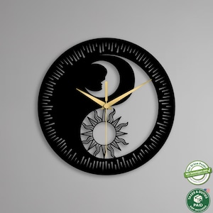 May include: Black Yin Yang wall clock with gold-colored hands. The clock features a sun and moon design with a silhouette of a person. The clock is round and has a detailed outer edge.