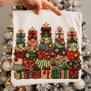 Pode incluir: Uma t-shirt branca com uma impressão gráfica de cinco árvores de Natal estilizadas decoradas com vários padrões, incluindo xadrez, bolinhas e riscas, rematadas com laços e estrelas, com caixas de presente na base de cada árvore.
