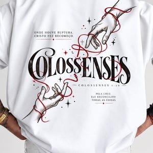 Pode incluir: Uma camiseta branca com um design gráfico de duas mãos estendidas uma para a outra, conectadas por um fio vermelho. O texto diz "COLOSSENSES", "ONDE HOUVE RUPTURA, CRISTO FEZ RECOMEÇO", "COLOSSENSES 1:20" e "PELA CRUZ, ELE RECONCILIOU TODAS AS COISAS."