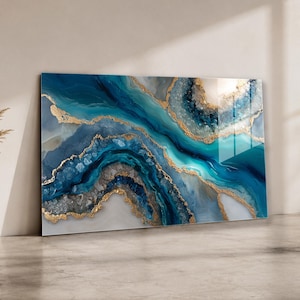Könnte beinhalten: Abstrakter Kunstdruck mit einem fließenden Design in Blau-, Türkis- und Weißtönen, akzentuiert durch goldfarbene Metallic-Linien. Das Kunstwerk hat eine glänzende Oberfläche und wird vor einer neutralen Wand ausgestellt.