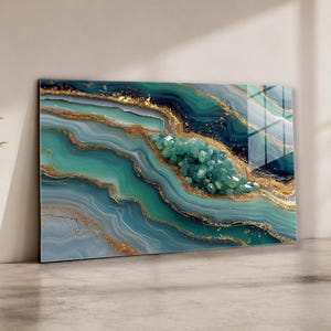 Puede incluir: Impresión artística abstracta con un diseño de geoda con acentos turquesa, azul y dorado. La obra de arte tiene un acabado brillante y está apoyada contra una pared de color neutro. El centro de la geoda está lleno de formaciones cristalinas.