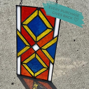 Könnte beinhalten: Buntglasfenster mit geometrischem Design. Das Panel zeigt rote, orange, gelbe, blaue und weiße Glasteile. Der Text "EVERY PURCHASE GIVES BACK" befindet sich auf einem türkisfarbenen Banner.