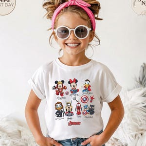 May include: A white t-shirt featuring Disney characters in superhero costumes. The shirt includes Mickey Mouse, Minnie Mouse, and Donald Duck, along with other characters and the word "Avengers". The child is wearing sunglasses and a pink headband.