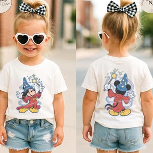 Op de afbeelding: Een kind draagt een wit t-shirt met een cartoonafbeelding van Mickey Mouse als tovenaar. Mickey, met een tovenaarsmuts, houdt een toverstaf vast. Het kind draagt ook een spijkerbroekshort en hartvormige zonnebrillen.