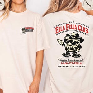 Puede incluir: Camiseta color crema con un gr&aacute;fico de un vaso de whisky de dibujos animados con sombrero de vaquero y gafas de sol. El texto "The Ella Fella Club" est&aacute; encima del gr&aacute;fico, con la frase "Choosin' Texas, I can tell." y un n&uacute;mero de tel&eacute;fono.