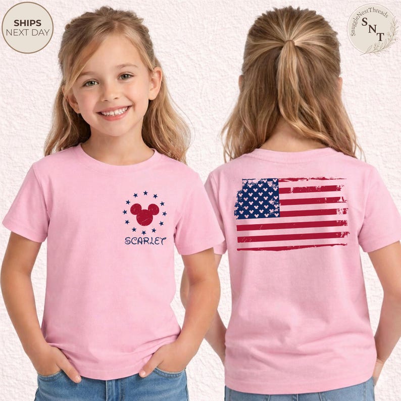 May include: A light pink t-shirt featuring a Mickey Mouse design surrounded by blue stars and the name "Scarlet" in blue. The back of the shirt displays a distressed American flag design in red, white, and blue.