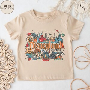 May include: Beige t-shirt featuring a colorful graphic of Disneyland Resort. The design includes various park icons, the Disneyland Resort logo, and the text "Ships Next Day". A fun and vibrant tee for Disney fans.