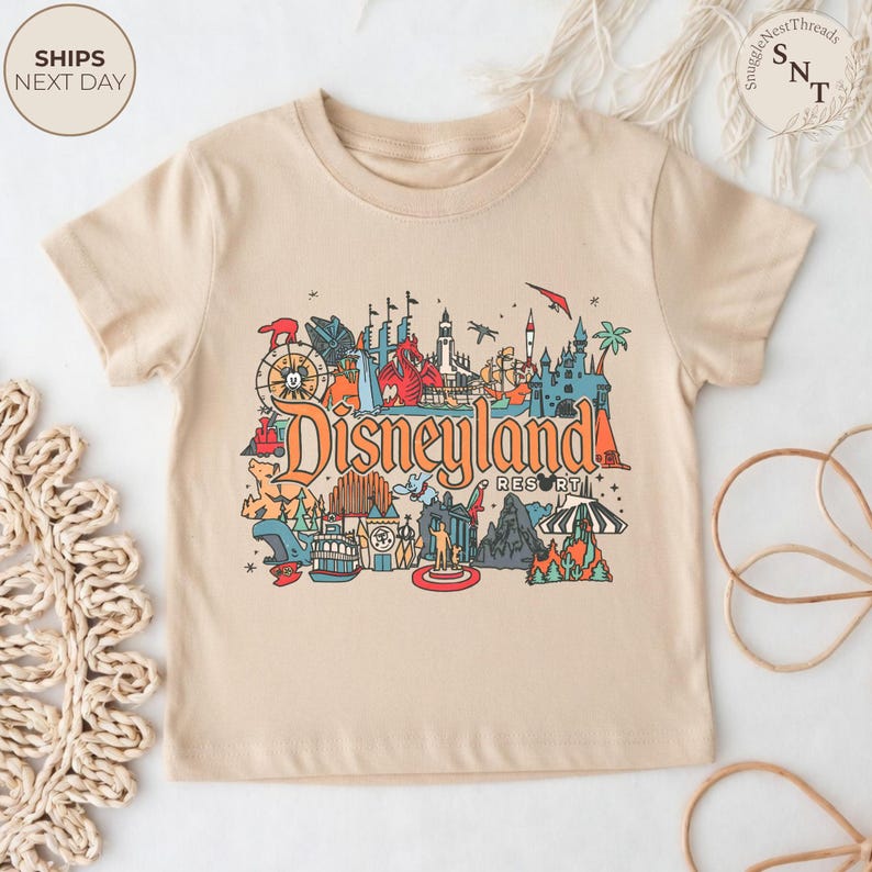 May include: Beige t-shirt featuring a colorful graphic of Disneyland Resort. The design includes various park icons, the Disneyland Resort logo, and the text "Ships Next Day". A fun and vibrant tee for Disney fans.