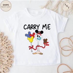 May include: White toddler t-shirt with the text "CARRY ME" in black. The shirt features a cartoon character holding balloons and a chocolate ice cream cone. The character is a spoon with a face and Mickey Mouse ears.