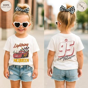 May include: A child wearing a white t-shirt with a Lightning McQueen graphic and denim shorts. The front of the shirt features the text "Lightning McQueen" and a race car design. The back displays the number "95" and "Lightning McQueen".