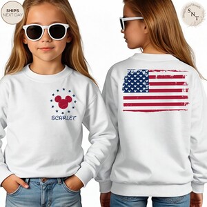 May include: White sweatshirt featuring a red and blue Mickey Mouse design surrounded by blue stars and the name "SCARLET". The back of the sweatshirt displays a distressed American flag. The sweatshirt is worn by a person wearing sunglasses.