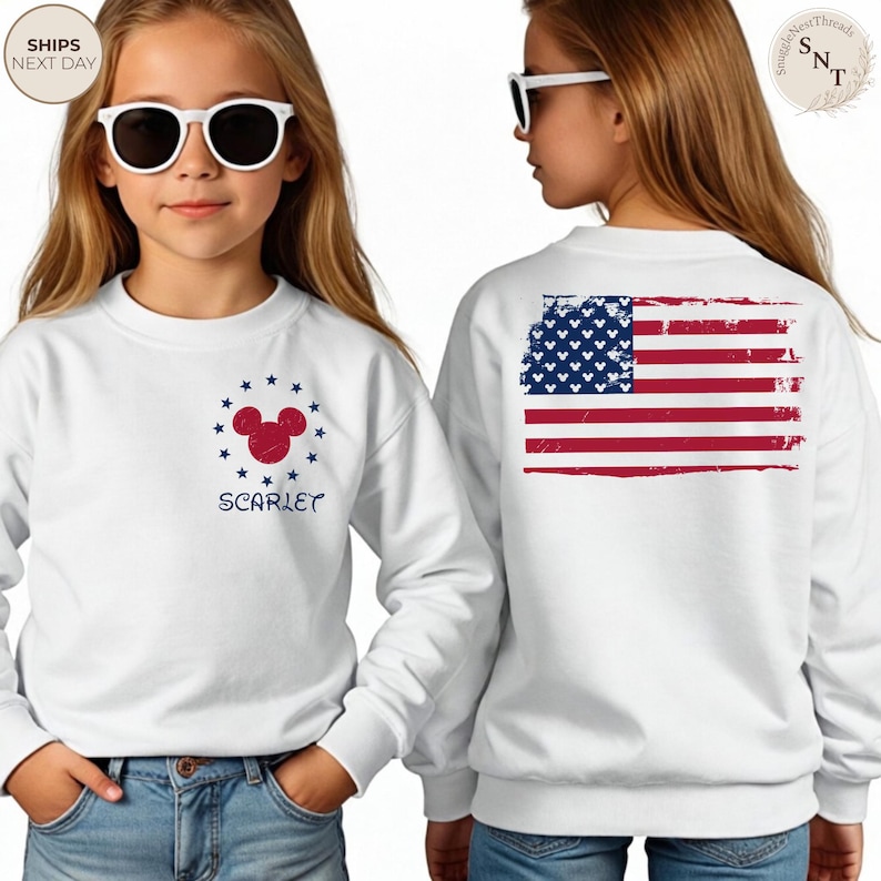 May include: White sweatshirt featuring a red and blue Mickey Mouse design surrounded by blue stars and the name "SCARLET". The back of the sweatshirt displays a distressed American flag. The sweatshirt is worn by a person wearing sunglasses.