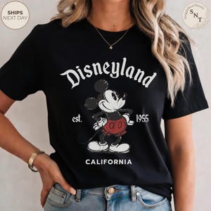 Pu&ograve; includere: T-shirt nero con grafica vintage di Disneyland. Il design include il logo Disneyland, Topolino e il testo "est. 1955 CALIFORNIA". La grafica &egrave; in bianco, rosso e nero.