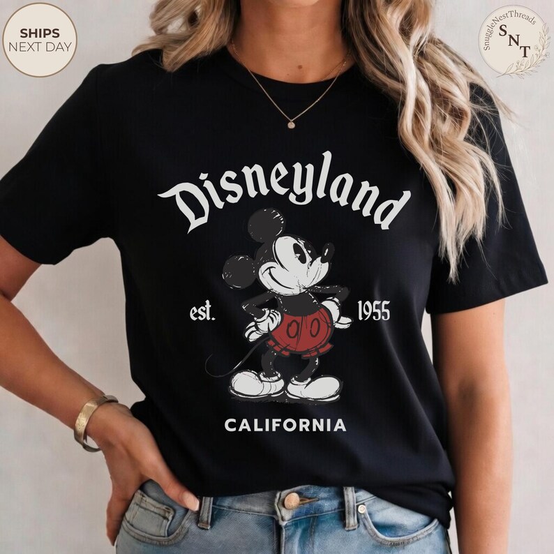 Pu&ograve; includere: T-shirt nero con grafica vintage di Disneyland. Il design include il logo Disneyland, Topolino e il testo "est. 1955 CALIFORNIA". La grafica &egrave; in bianco, rosso e nero.