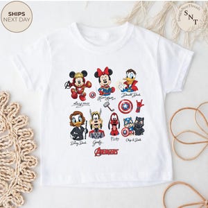 May include: White t-shirt featuring a colorful graphic of Disney characters in Avengers-themed designs. Characters include Mickey Mouse, Minnie Mouse, Donald Duck, Daisy Duck, Goofy, Pluto, Chip and Dale. The word "Avengers" is printed in red.