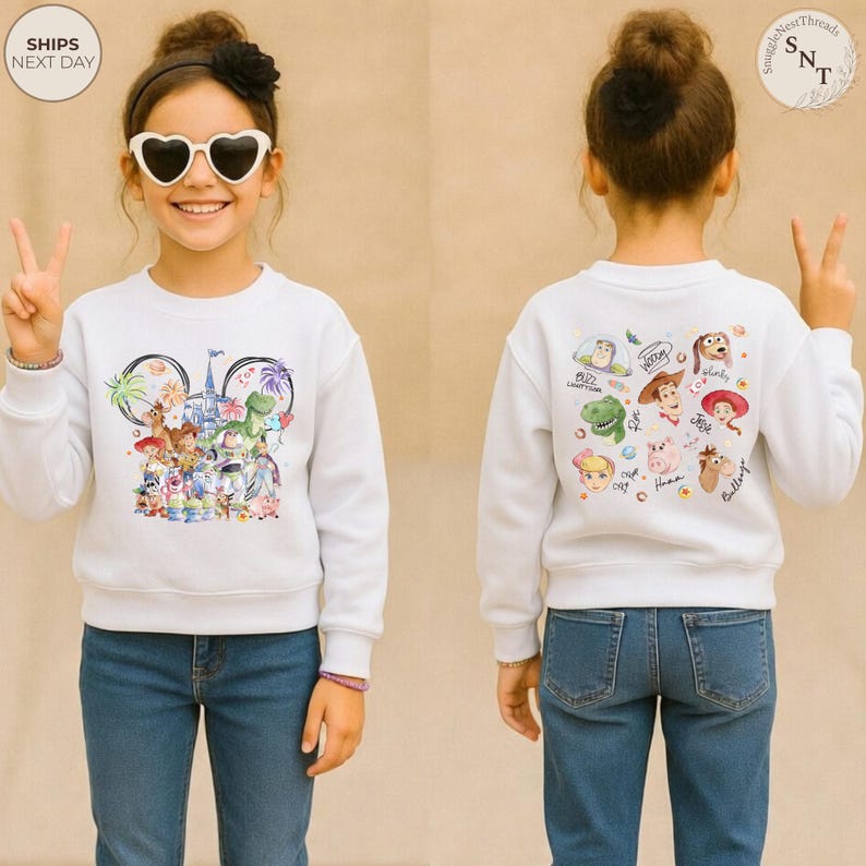 Puede incluir: Una sudadera blanca de manga larga con un gr&aacute;fico frontal de varios personajes animados dispuestos en forma de orejas de Mickey Mouse con un castillo y fuegos artificiales, y un gr&aacute;fico trasero con caras y nombres de personajes.