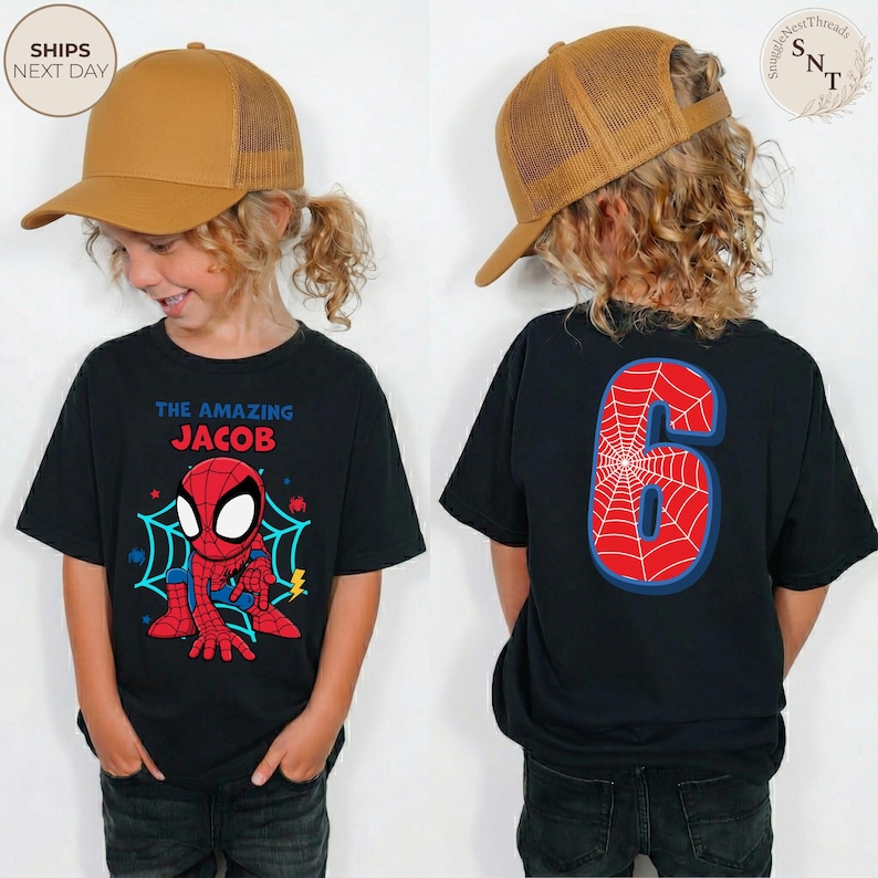 Puede incluir: Camiseta negra con un dise&ntilde;o de Spider-Man y el texto "THE AMAZING JACOB" en la parte delantera. La parte trasera de la camiseta muestra un gran n&uacute;mero "6" con un dise&ntilde;o de telara&ntilde;a. El ni&ntilde;o lleva una gorra de camionero marr&oacute;n.