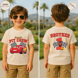 May include: A tan t-shirt featuring a red race car graphic with the text "David's PIT CREW" and checkered flags. The back of the shirt says "BROTHER" above a red number 1 with a race car and checkered flags. The boy is wearing sunglasses.