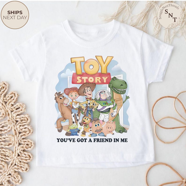K&ouml;nnte beinhalten: Wei&szlig;es T-Shirt mit dem Toy Story-Logo und -Charakteren. Das Design zeigt Woody, Buzz Lightyear und andere Charaktere aus dem Film. Der Text "YOU'VE GOT A FRIEND IN ME" ist darunter gedruckt.