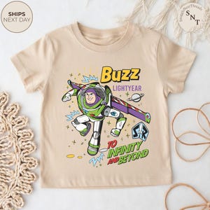 Puede incluir: Camiseta beige con un gr&aacute;fico colorido de Buzz Lightyear de Toy Story. El dise&ntilde;o incluye el texto "Buzz Lightyear" y "To Infinity and Beyond". La camiseta tiene mangas cortas y cuello redondo.