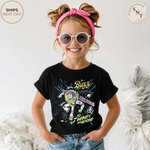 Puede incluir: Una camiseta negra con un gr&aacute;fico de Buzz Lightyear de Toy Story. El dise&ntilde;o incluye el texto "Buzz Lightyear" y "To Infinity and Beyond". La camiseta la lleva un ni&ntilde;o con una diadema rosa y gafas de sol.