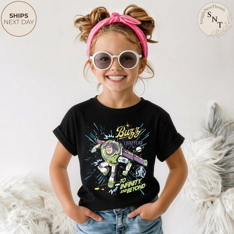 Puede incluir: Una camiseta negra con un gr&aacute;fico de Buzz Lightyear de Toy Story. El dise&ntilde;o incluye el texto "Buzz Lightyear" y "To Infinity and Beyond". La camiseta la lleva un ni&ntilde;o con una diadema rosa y gafas de sol.