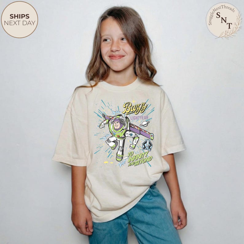 Puede incluir: Camiseta color crema con un gr&aacute;fico de Buzz Lightyear, con el texto "Buzz Lightyear" y "To Infinity and Beyond". El dise&ntilde;o incluye detalles en verde, morado y azul. La camiseta la lleva una persona joven.