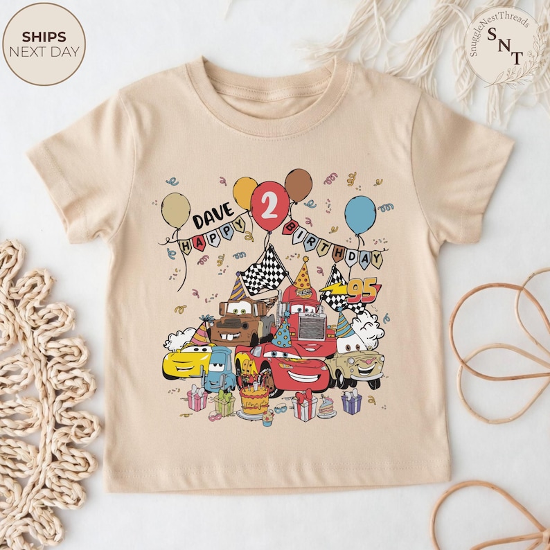 Puede incluir: Una camiseta beige para ni&ntilde;os peque&ntilde;os con un gr&aacute;fico colorido de coches de dibujos animados celebrando un cumplea&ntilde;os. El dise&ntilde;o incluye globos, una tarta de cumplea&ntilde;os y el texto "DAVE HAPPY BIRTHDAY 2".