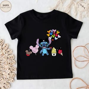 Pu&ograve; includere: T-shirt nera con un personaggio dei cartoni animati Stitch che tiene in mano palloncini di Topolino colorati, zucchero filato e gelato. Il design &egrave; colorato e adatto ai bambini.
