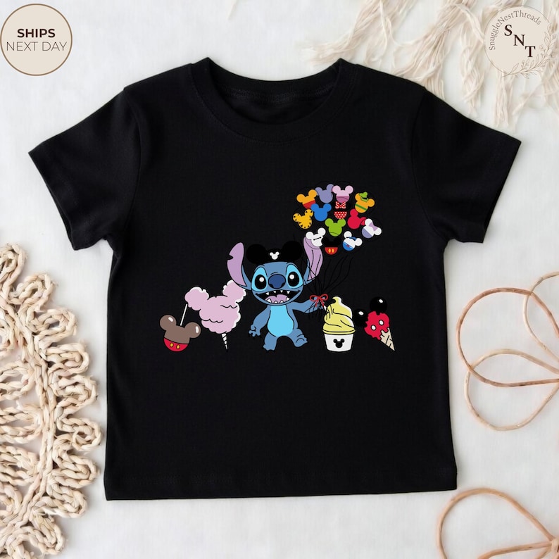 Pu&ograve; includere: T-shirt nera con un personaggio dei cartoni animati Stitch che tiene in mano palloncini di Topolino colorati, zucchero filato e gelato. Il design &egrave; colorato e adatto ai bambini.