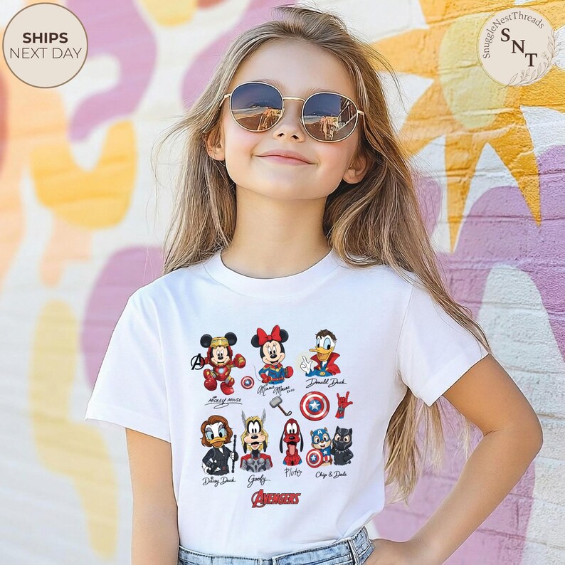 May include: A white t-shirt featuring cartoon characters including Mickey Mouse, Minnie Mouse, and Donald Duck, with the word "AVENGERS" at the bottom. The shirt is worn by a young person wearing sunglasses.