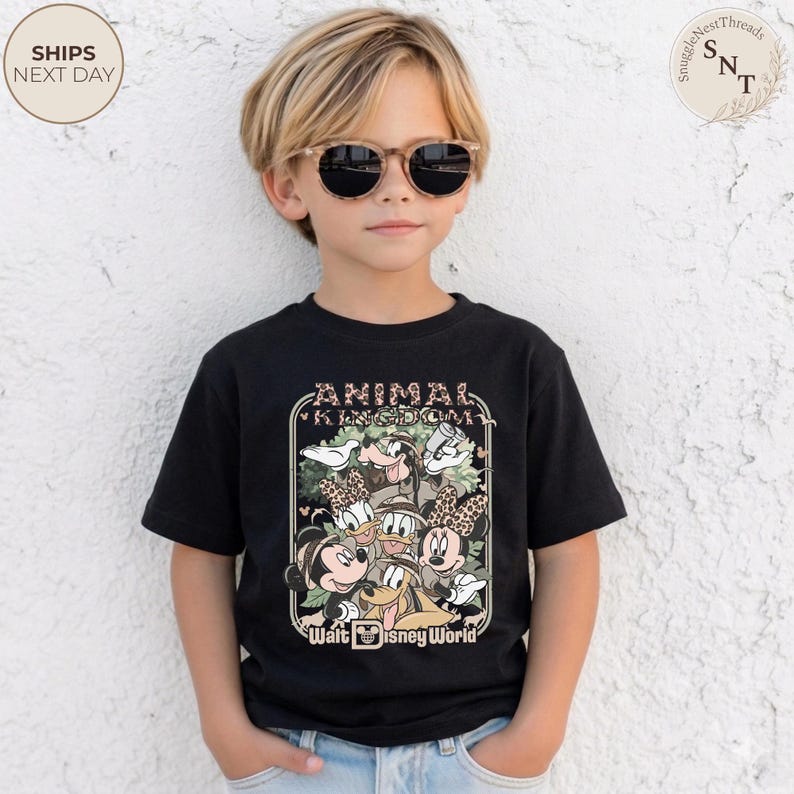 Pu&ograve; includere: T-shirt nero con una grafica colorata dei personaggi Disney, tra cui Topolino e Minnie, Paperino e Paperina, e Pippo. La maglietta presenta la scritta "ANIMAL KINGDOM" e "Walt Disney World".