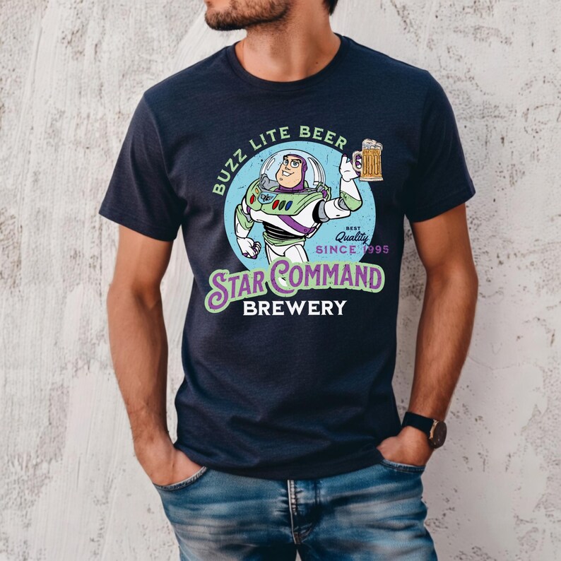 Puede incluir: Camiseta azul marino con un dise&ntilde;o de dibujos animados de Buzz Lightyear sosteniendo una jarra de cerveza. El dise&ntilde;o incluye el texto "Buzz Lite Beer" y "Star Command Brewery" con "Best Quality Since 1995". La camiseta es de cuello redondo.