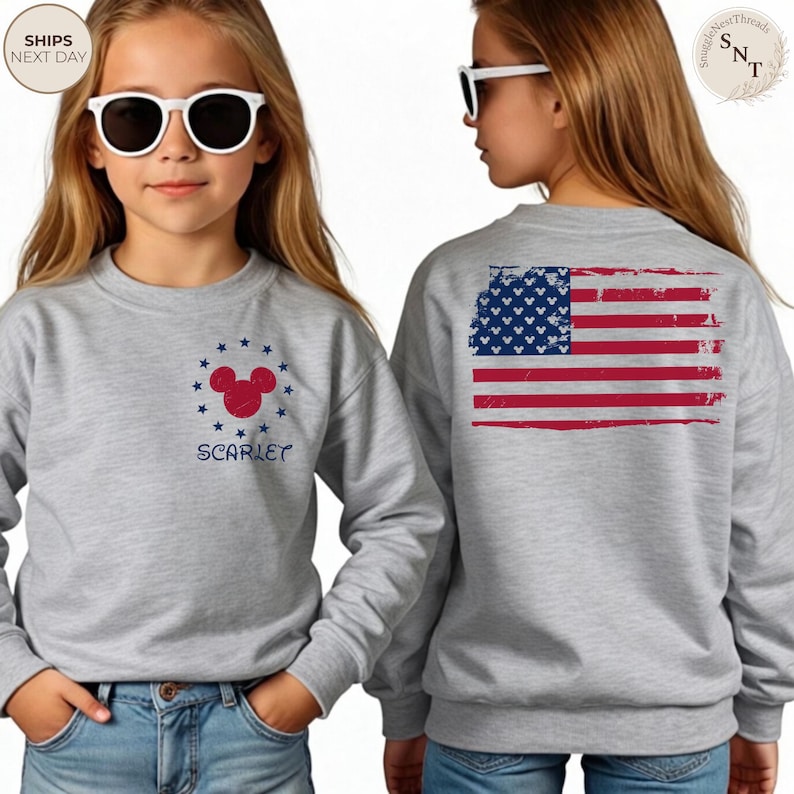 May include: A gray sweatshirt featuring a Mickey Mouse design with stars and the name "Scarlet" in navy blue. The back of the sweatshirt displays a distressed American flag design in red, white, and blue.