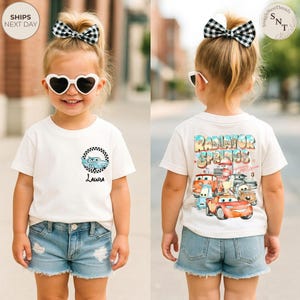 May include: A cream-colored t-shirt featuring a cartoon car design with the name "Laura" below it. The back of the shirt displays a "Radiator Springs" graphic with various car characters. The child is wearing denim shorts and heart-shaped sunglasses.