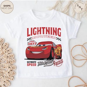 Op de afbeelding: Witte t-shirt met een Lightning McQueen-ontwerp. De rode raceauto-afbeelding wordt vergezeld door de tekst "LIGHTNING MCQUEEN", "est. 1977", "ULTIMATE SPEED" en "Think Fast". Een kledingstuk voor kinderen.